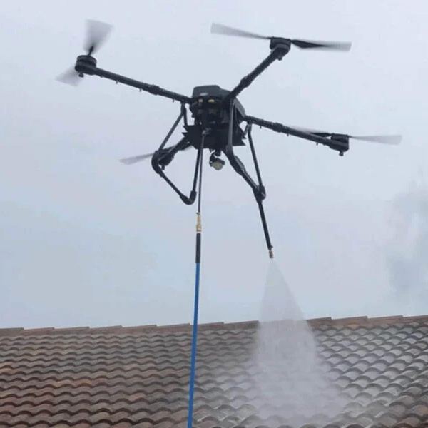 Drone met een blauwe waterslang sproeit water over een dak met rode dakpannen
